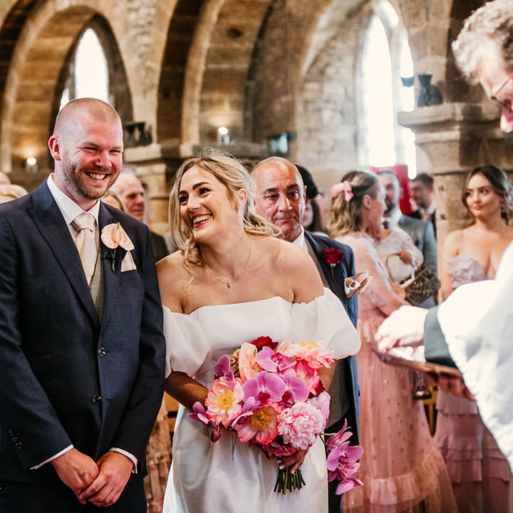 Groom in dark navy suit with pale pink anthurium buttonhole laughing with the bride at their church ceremony in the bride's hometown 