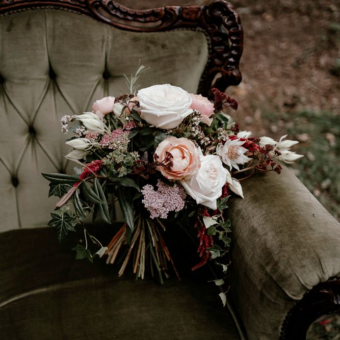 Blush pink and white wedding bouquet resting on a vintage couch 