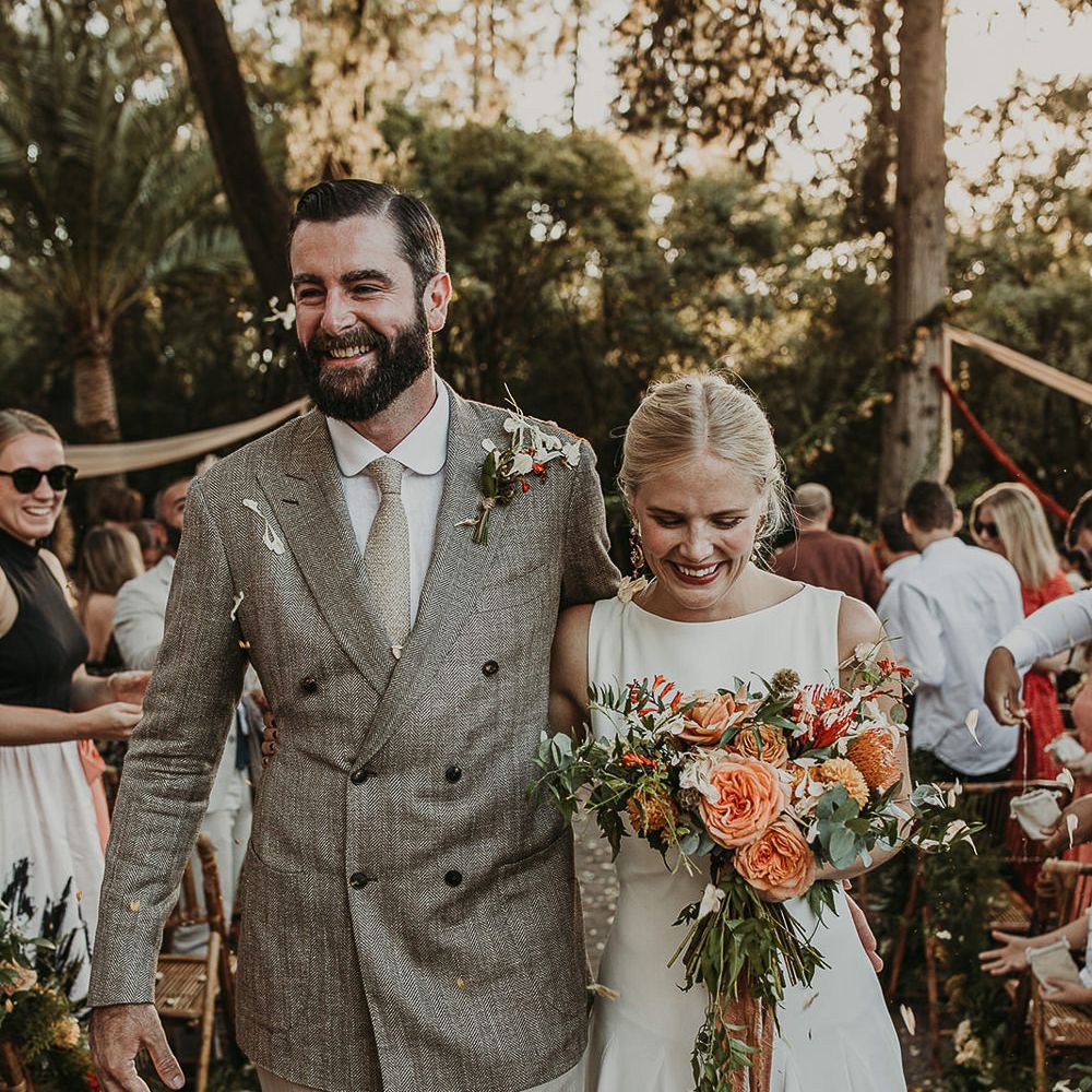 Bride holding a bouquet with coral flowers and groom wearing a double breasted jacket 