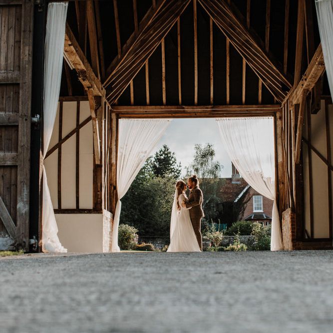 Beautiful barn wedding photography with the bride and groom holding each other in the barn doorway 