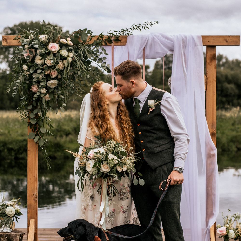 Bride & groom with their dog under floral arch 
