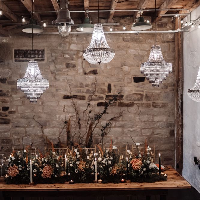 Intimate wedding reception with wooden table, chandelier light installation and foliage and flower table flowers