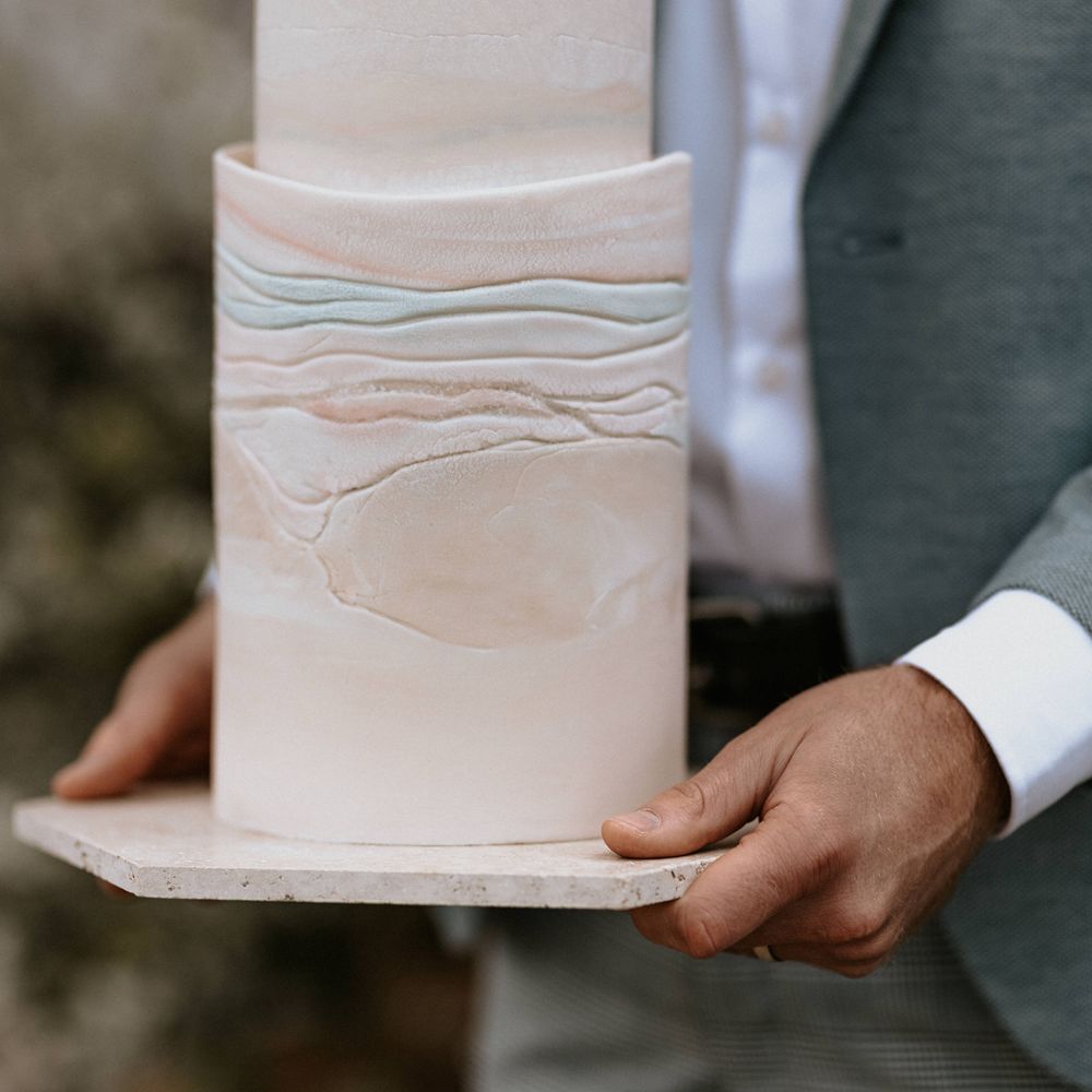 Groom holds contemporary wedding cake with pastel colouring