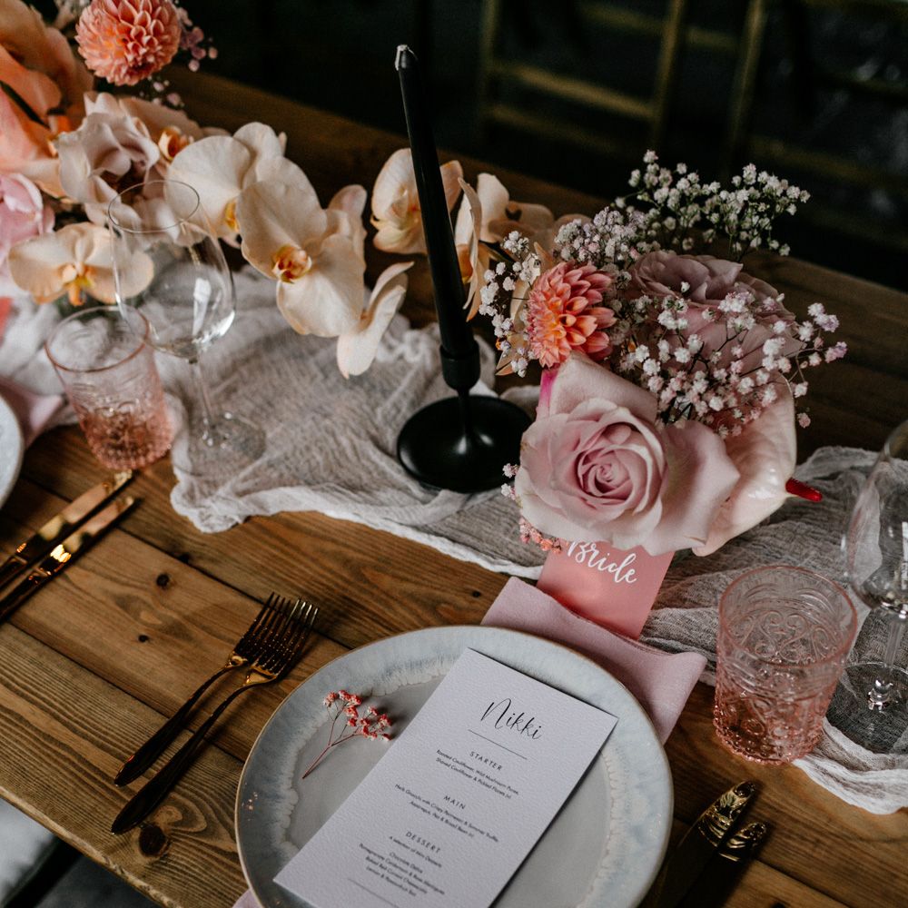 Place setting with gold cutlery and coloured glassware, plus peel back rose centrepieces and black taper candles 