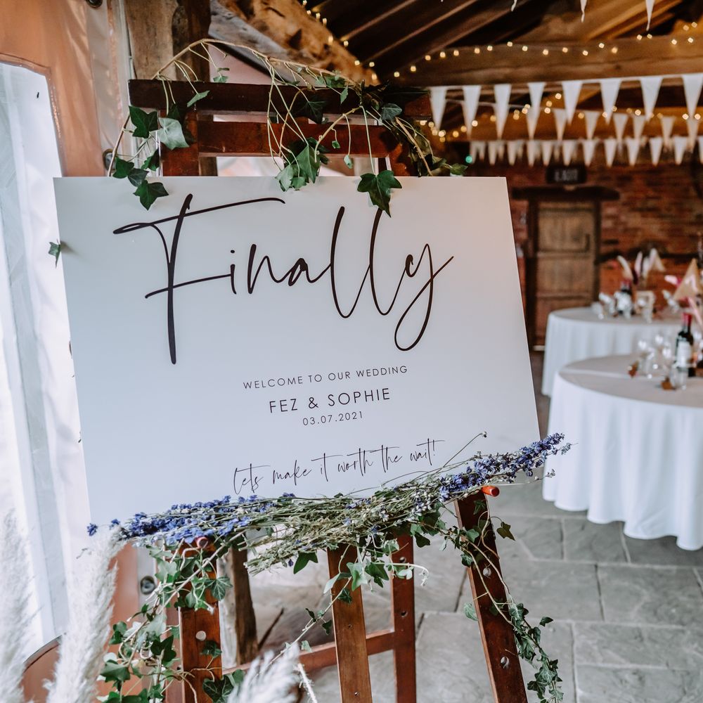 Rustic barn wedding venue complete with white sign surrounded by florals