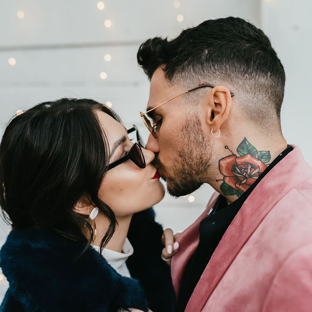 Groom in a pink velvet jacket kissing his bride in a navy blue faux fur coat and sunglasses 