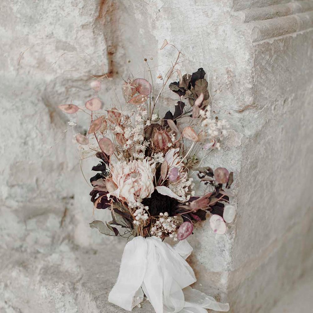 dried flower stem wedding bouquet in neutral and blush tones resting against a wall