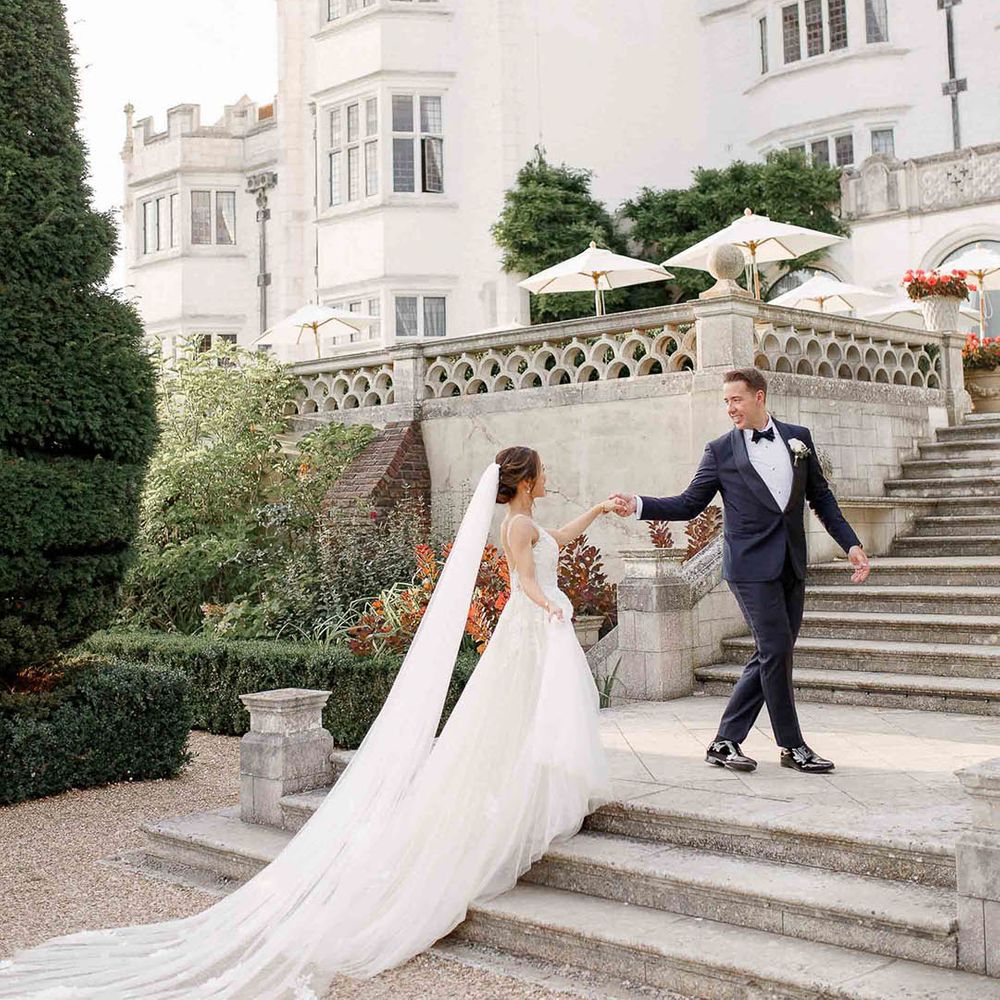 Groom leads his bride up grand staircase outdoors at Danesfield House