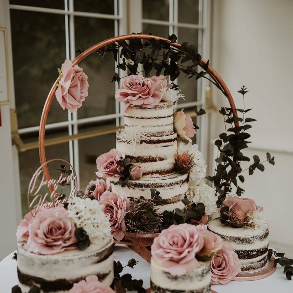 Table complete with four naked wedding cakes with white frosting and covered in pink roses 