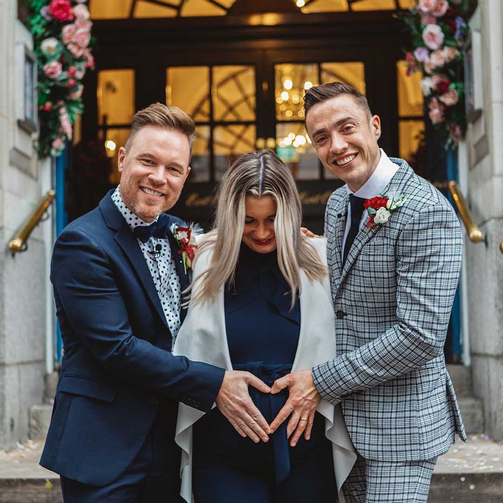 Grooms place their hands in a heart shape on surrogates belly