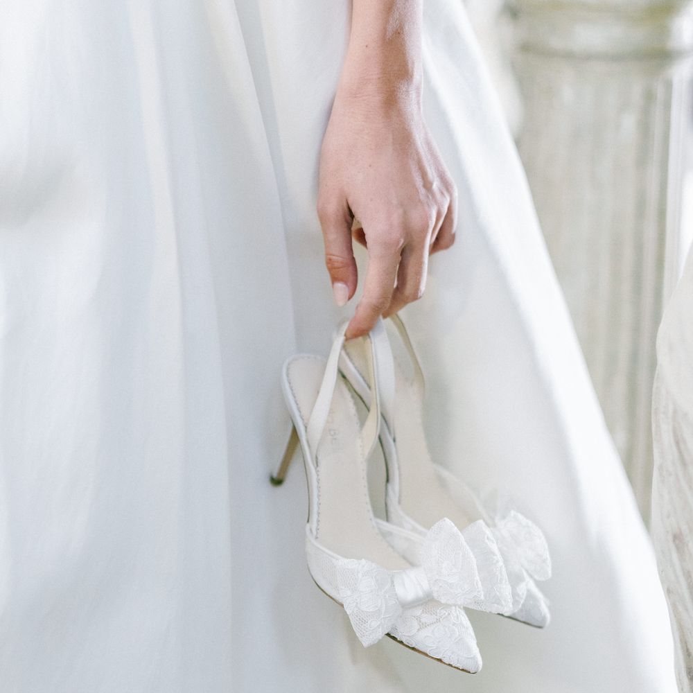 Bride in white dress holding the sheer lace wedding court shoes with bow