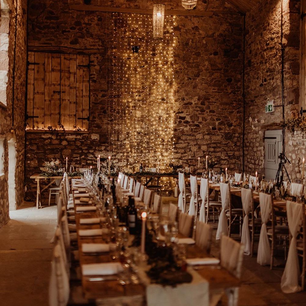 Rustic Eden Barn wedding venue with fairy lights, white tablecloth banquet tables, white wedding drape chair back decor 
