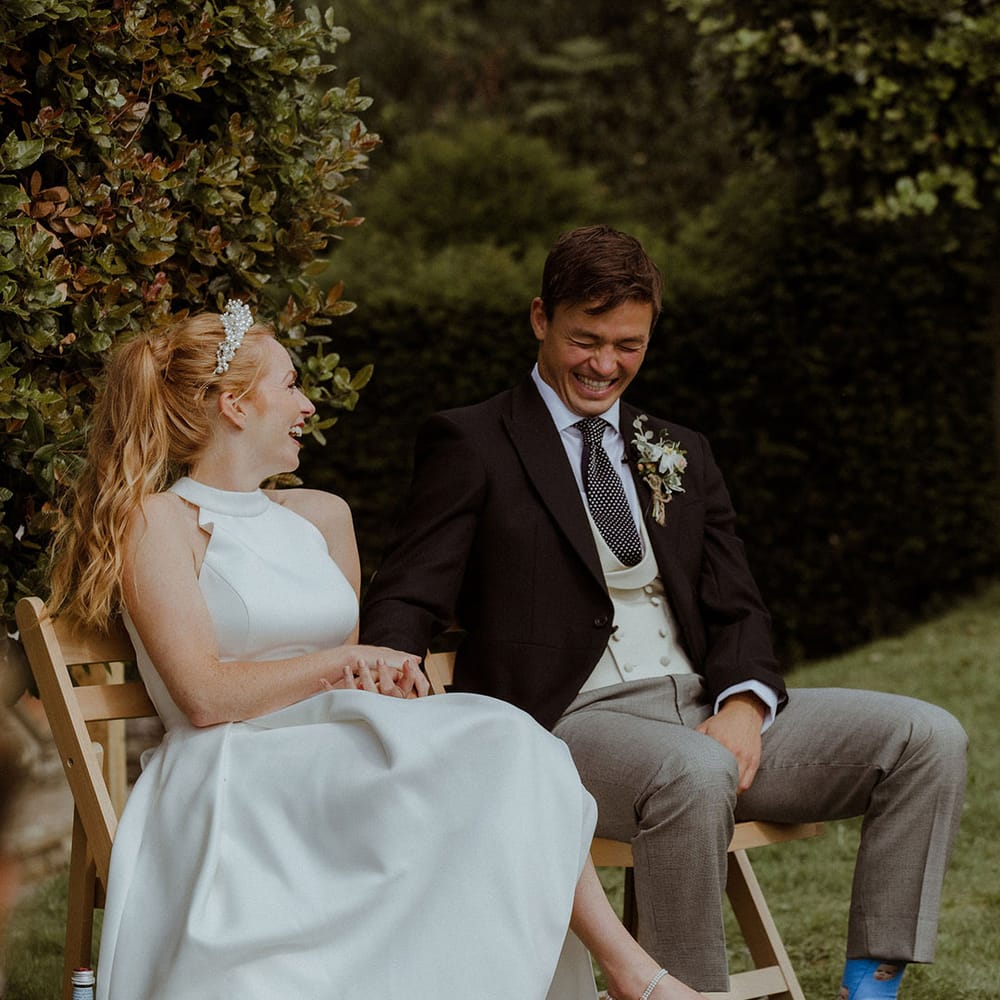 Bride in halter neck wedding dress with pearl embeliished wedding shoes and pearl headband laughing with groom in morning suit 