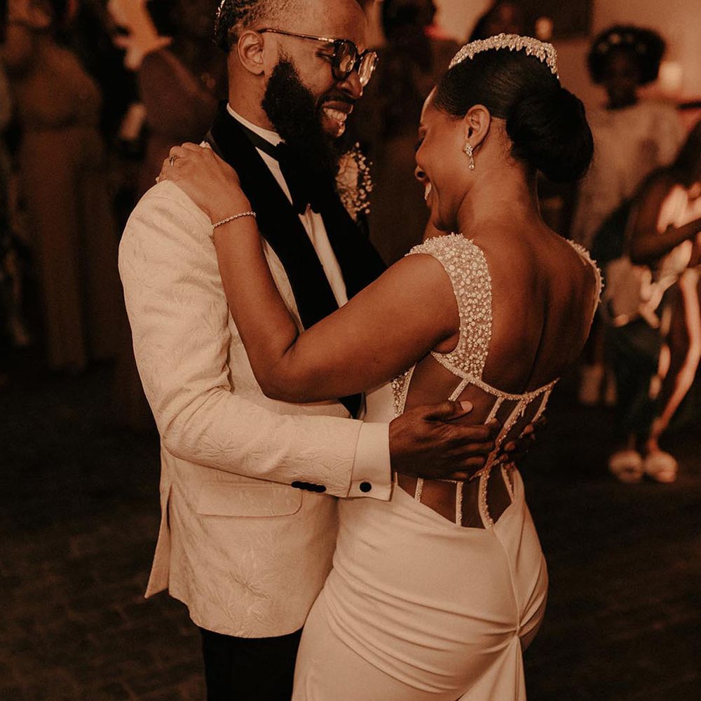 Bride in pearl detail open back wedding dress and groom in white tux doing their first dance