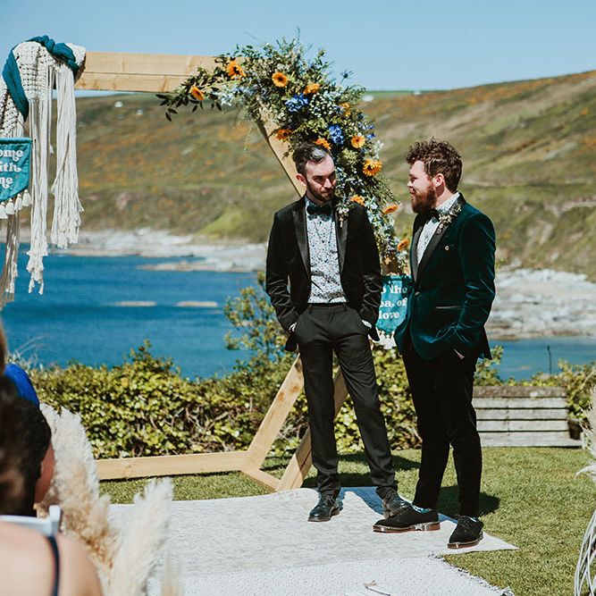Groom wears green velvet suit jacket and stands beside groomsmen who wears black velvet dinner jacket 