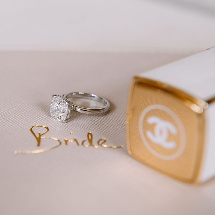 Silver engagement ring with square diamond on Bride bag next to Chanel lipstick 