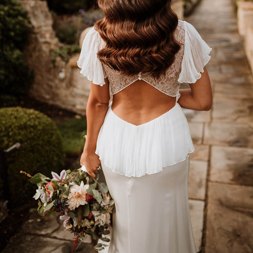 Bride in satin open back wedding dress with button details and butterfly sleeves, ruffled and layer on the back
