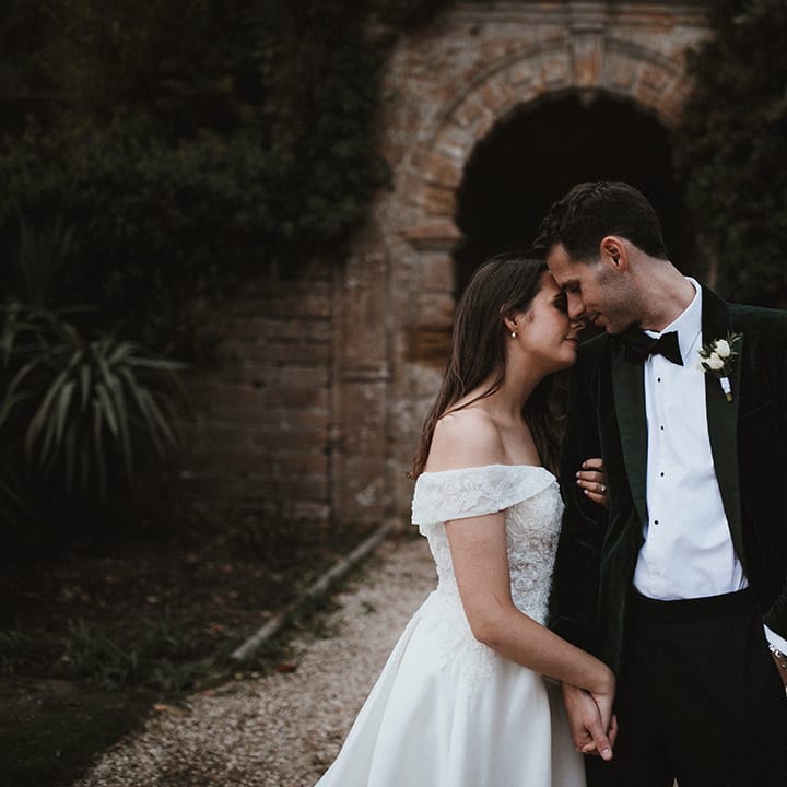 Bride in off the shoulder wedding dress smiling with the groom in a dark green velvet tuxedo for timeless traditional wedding 