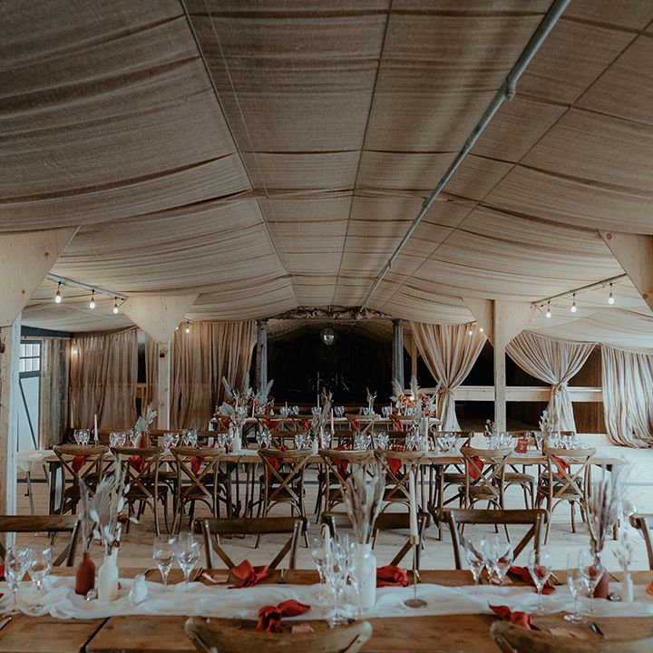 Rustic glam Rhyse Farm wedding venue with wooden tables with white table runners, orange napkins and bunny grass floral arrangements 