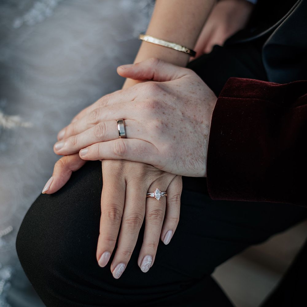 The groom wears a plain silver wedding band with the bride wearing rose gold engagement ring and silver wedding band 