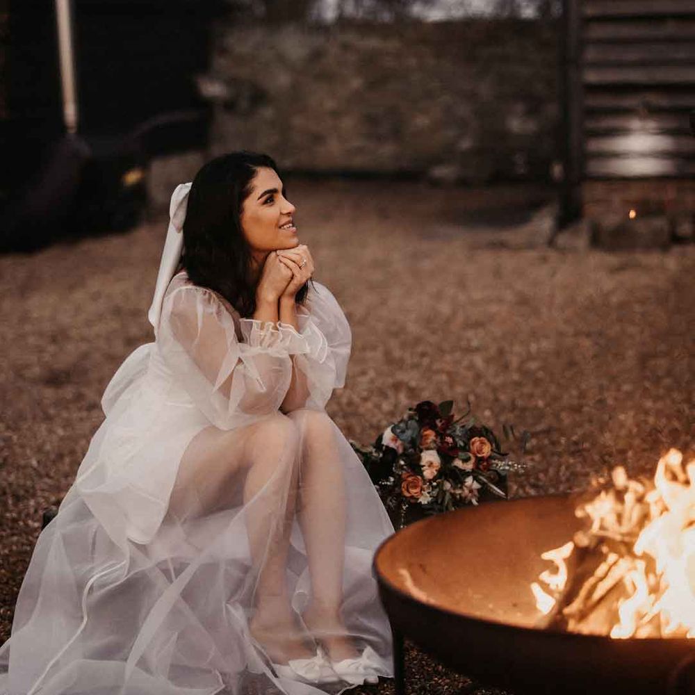 Bride in sheer overlay puff sleeve wedding dress and strapless wedding heels sitting by the fire pit 