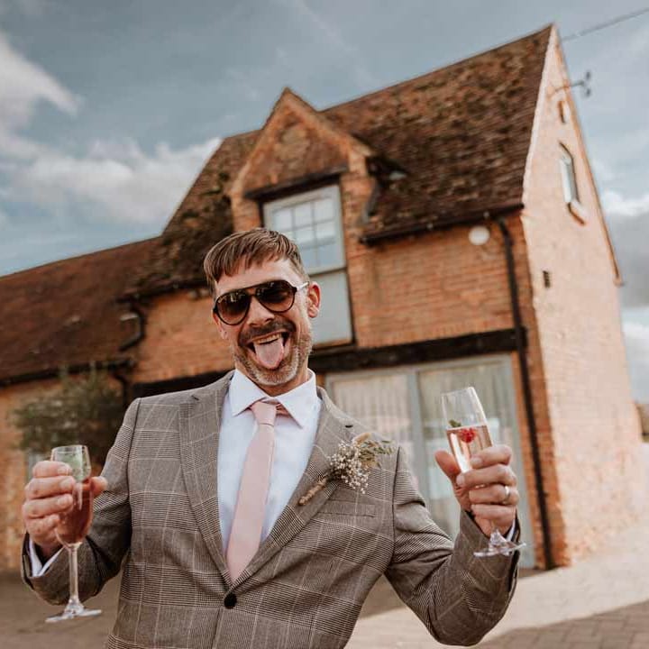 Wedding guest in light grey checkered suit, pink tie and dried flower autumnal boutonniere 