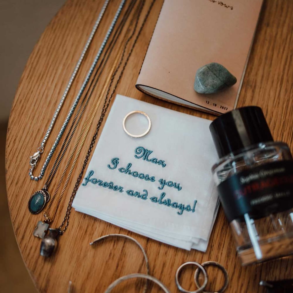 Embroidered ivory and turquoise grooms pocket square with silver and gold grooms wedding jewellery on wooden table 