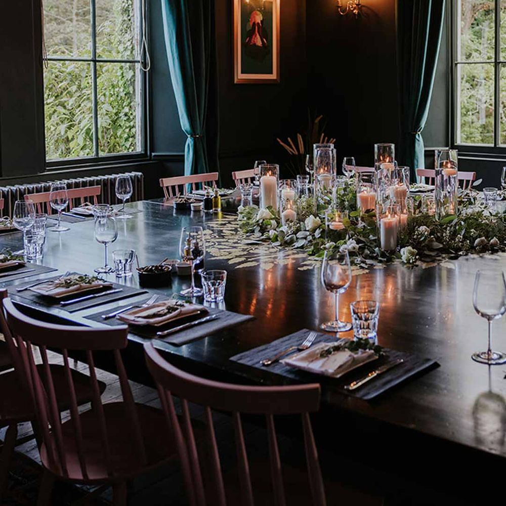 Reception room of Netherbyres House Scottish wedding venue with dark tones, gold framed alternative wedding photos and windows overlooking manicured lawns 
