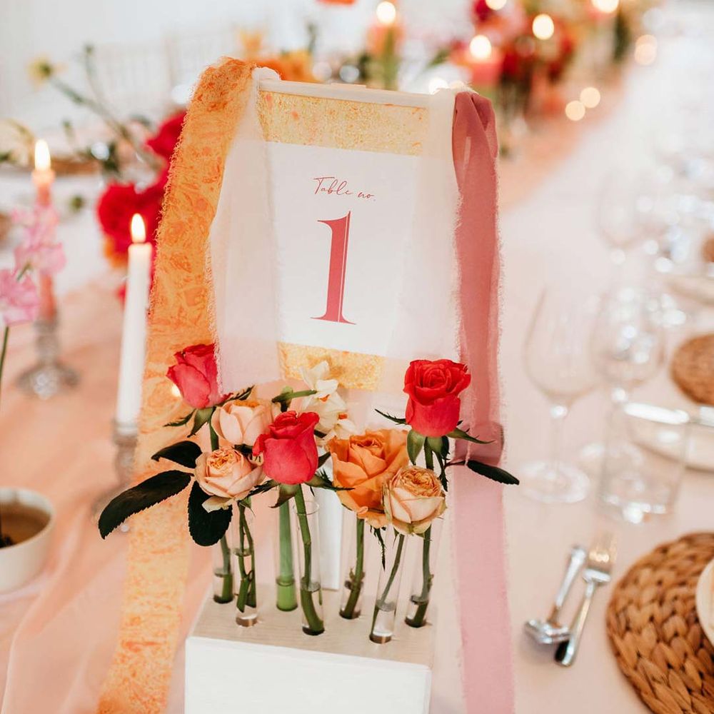 Colourful alternative wedding table number with frayed orange and pink ribbon and test tube vase holders with garden roses 