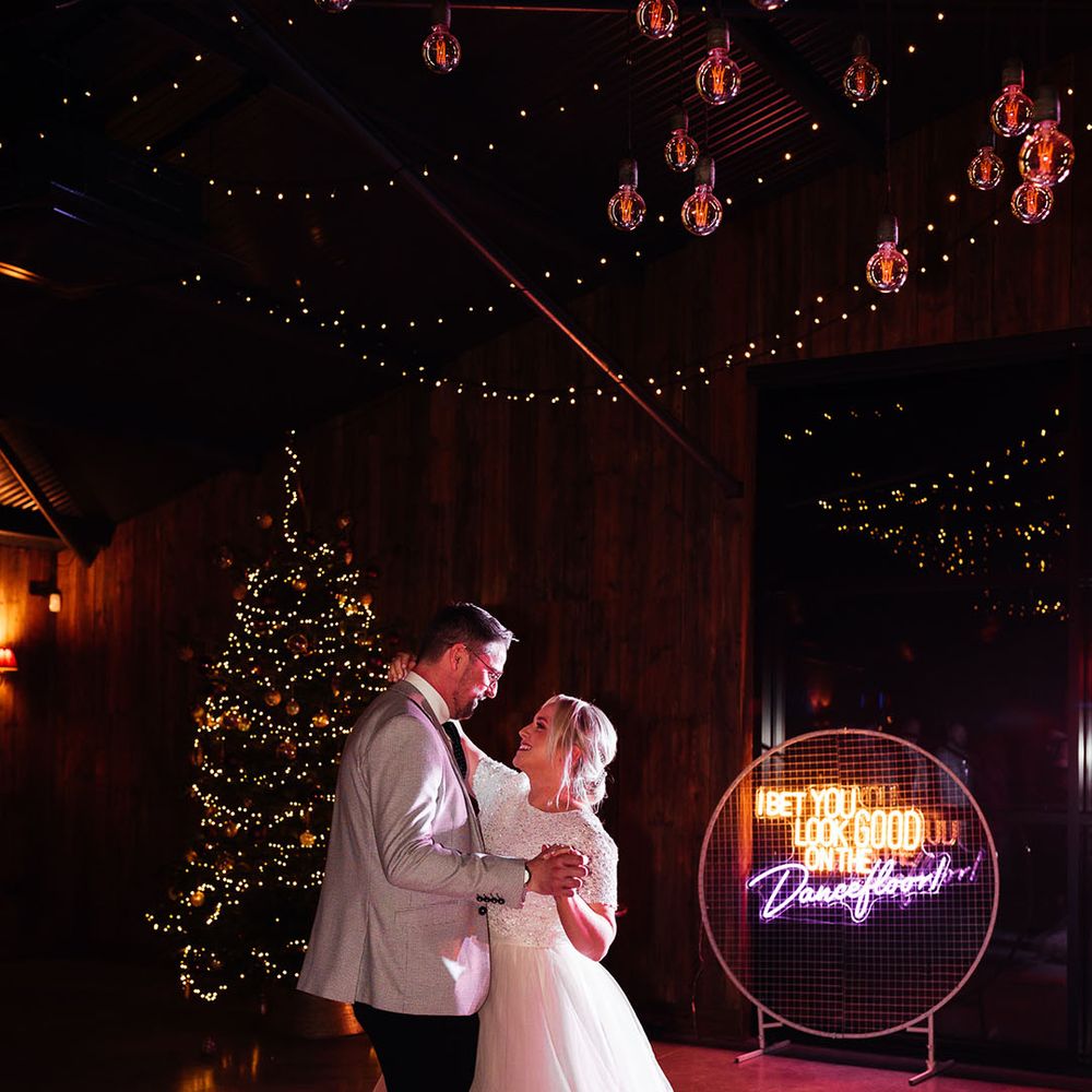 The bride and groom share their first dance together on the checkered dance floor with a Christmas tree festive decoration 