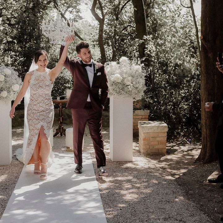 Bride in Grace Loves Lace wedding dress with groom in burgundy suit walking back down the aisle as a married couple 