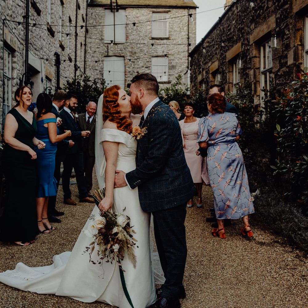 Bride with vintage wedding hair kissing her groom at the end of the confetti exit 