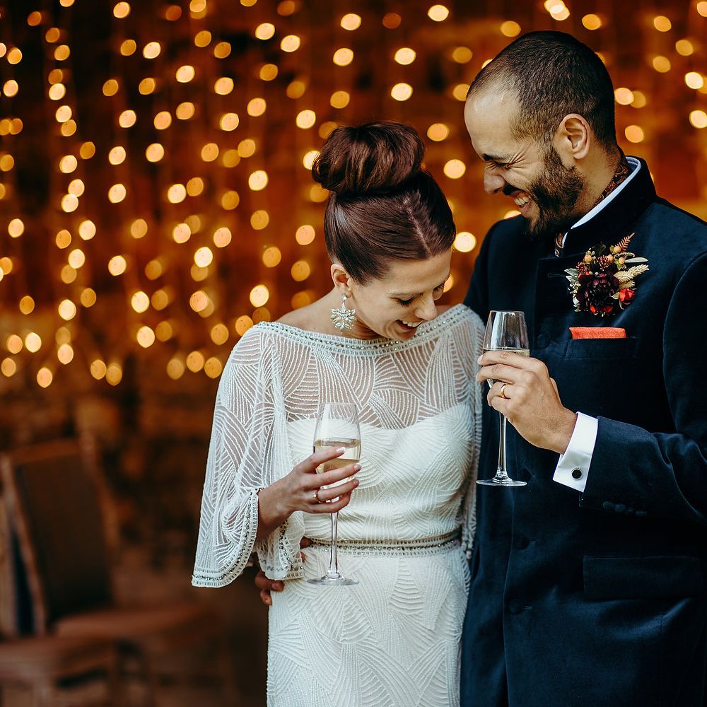 Bride & groom stand in front of twinkling fairy lights