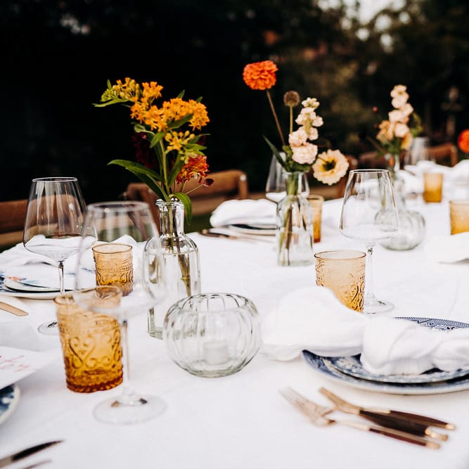 Wedding table decor with yellow goblets, blue tableware and flower stems in bottles 