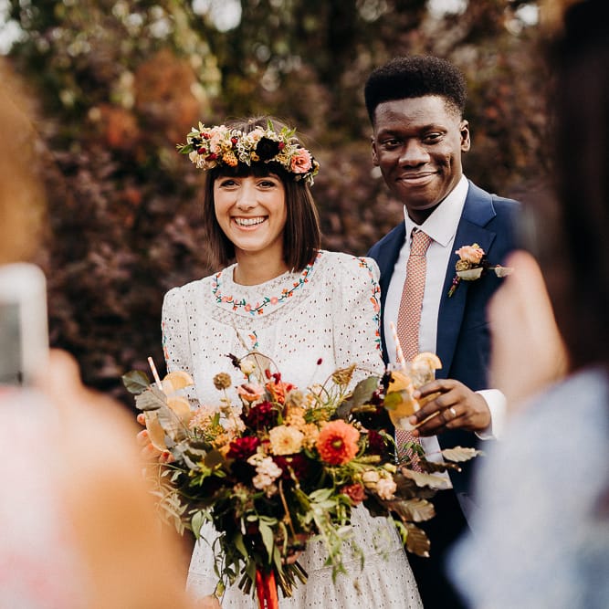 Bride and groom smiling during the drinks reception with the bride wearing a colourful flower crown and holding a wildflower bouquet 