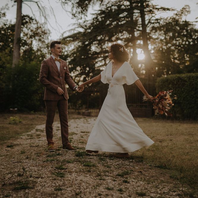 Groom in a brown wedding suit twirling his bride during golden hour in a minimalist wedding dress 