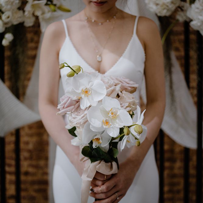 Bride in a minimalist wedding dress holding a white orchid wedding bouquet 