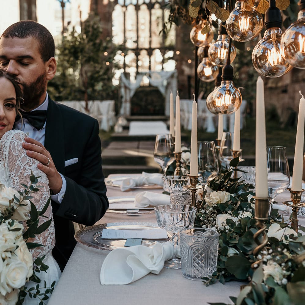 Bride and groom sitting at their elegant green, gold and glass wedding reception table in black tie attire 