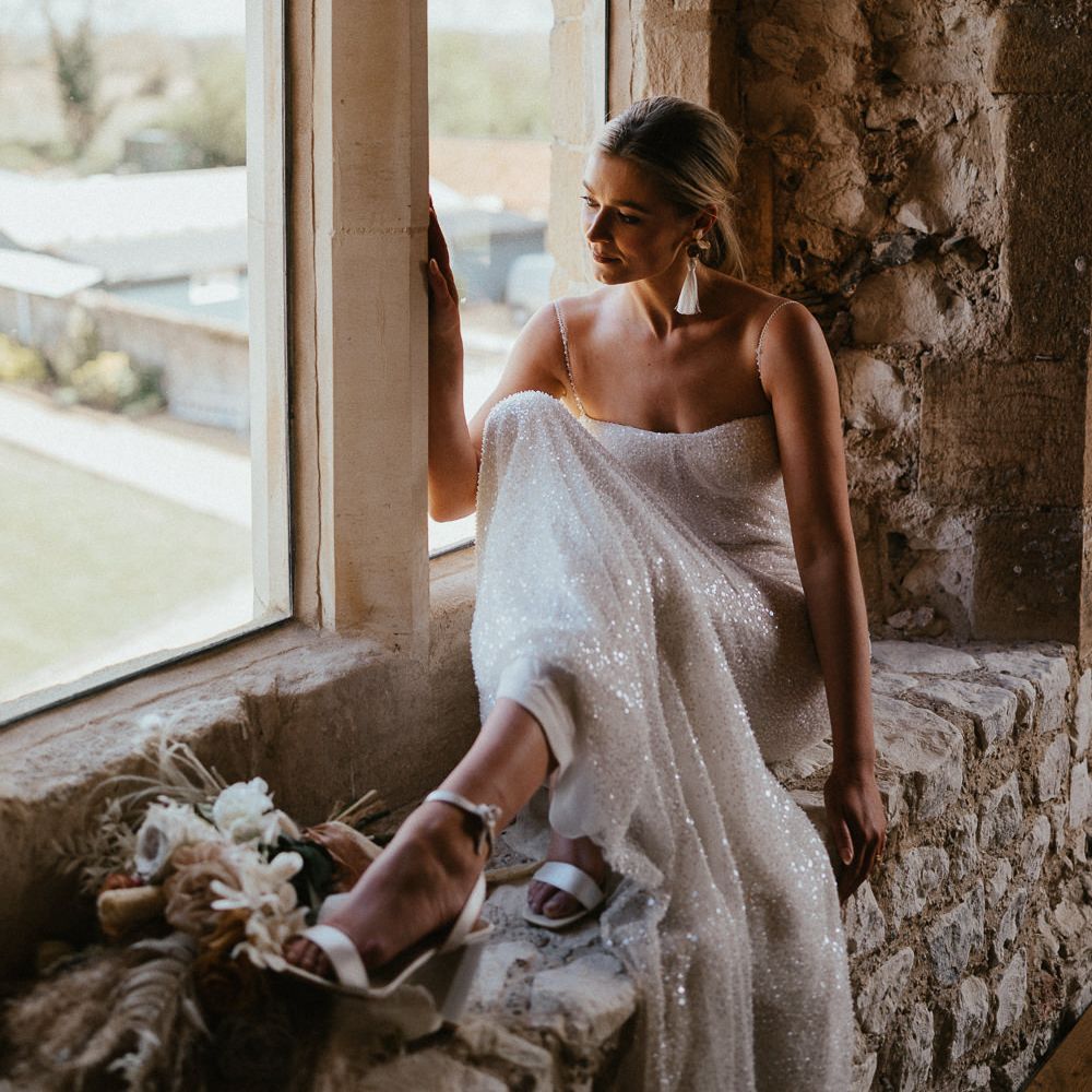 Bride in a white embellished wedding dress with thin straps and tassel earrings