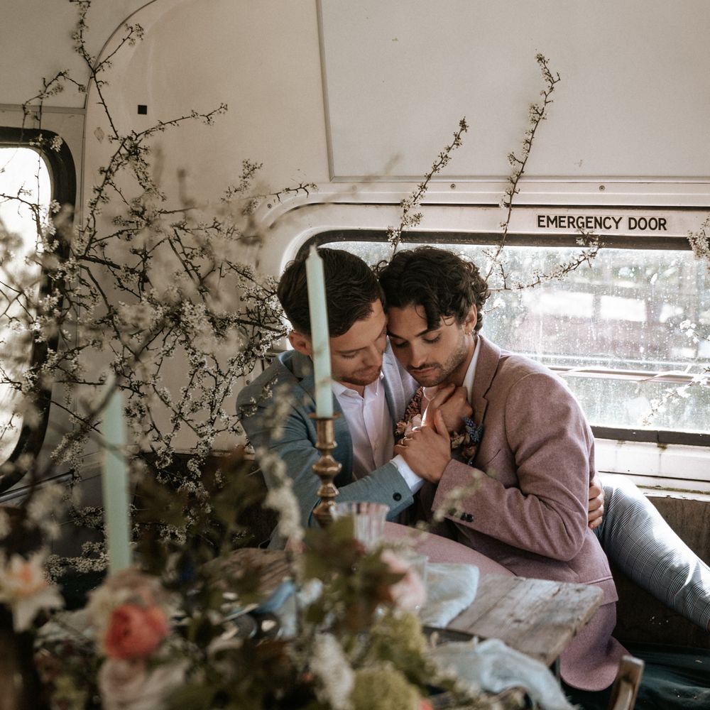 Grooms sit closely with one another on their wedding day whilst wearing pastel suits