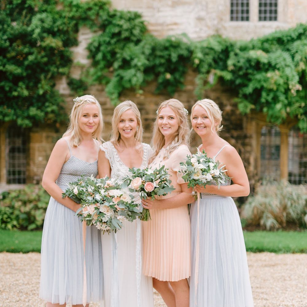 Bride in white dress holding bouquet in portrait with three bridesmaids in pastel blue and peach dresses