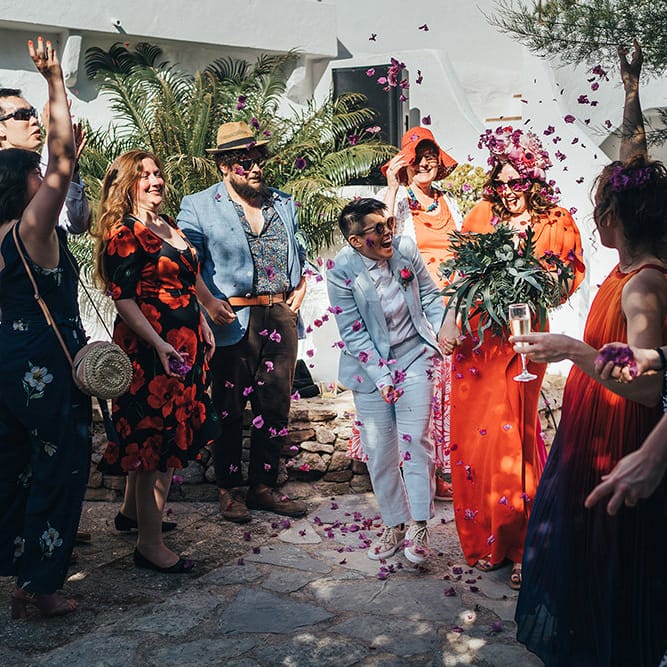 Brides walk through pink confetti on their wedding day after marrying