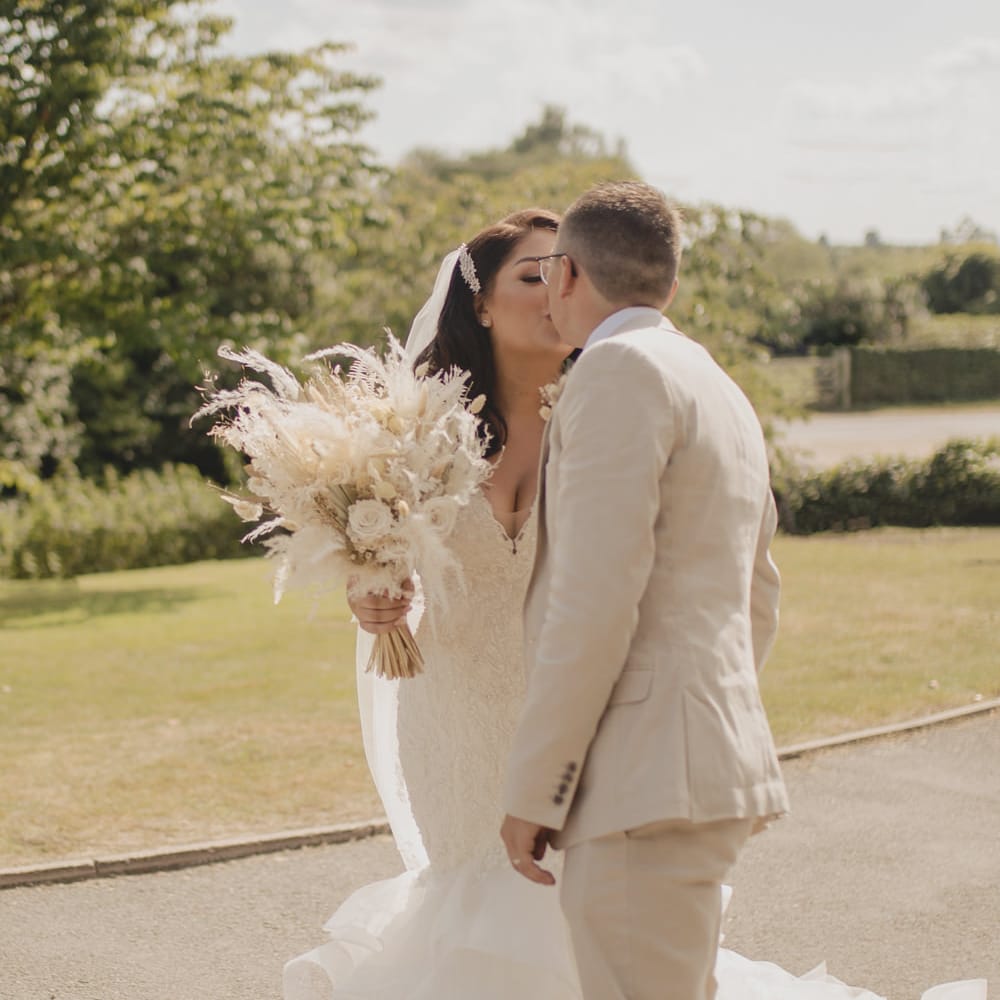 Groom in a beige linen suit kissing his bride in a fitted lace wedding dress with fishtail skirt 