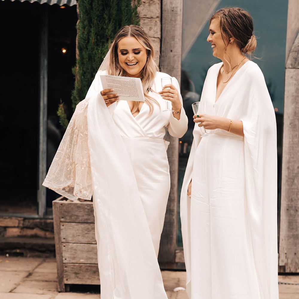 Brides stand with one another outdoors in their white bridal jumpsuits
