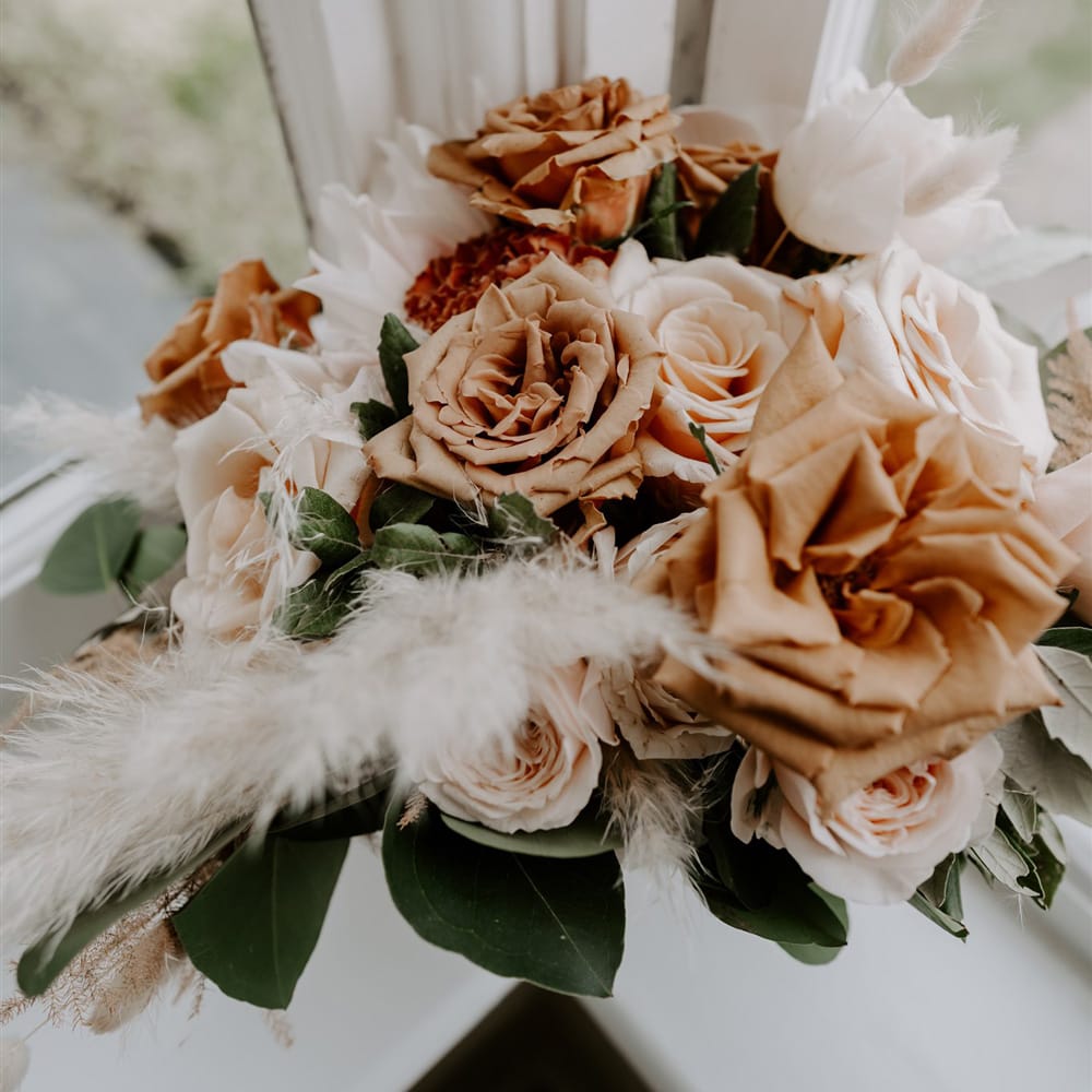 Dusky orange, and blush pink roses with green foliage and dried grass bridal bouquet for DIY garden wedding