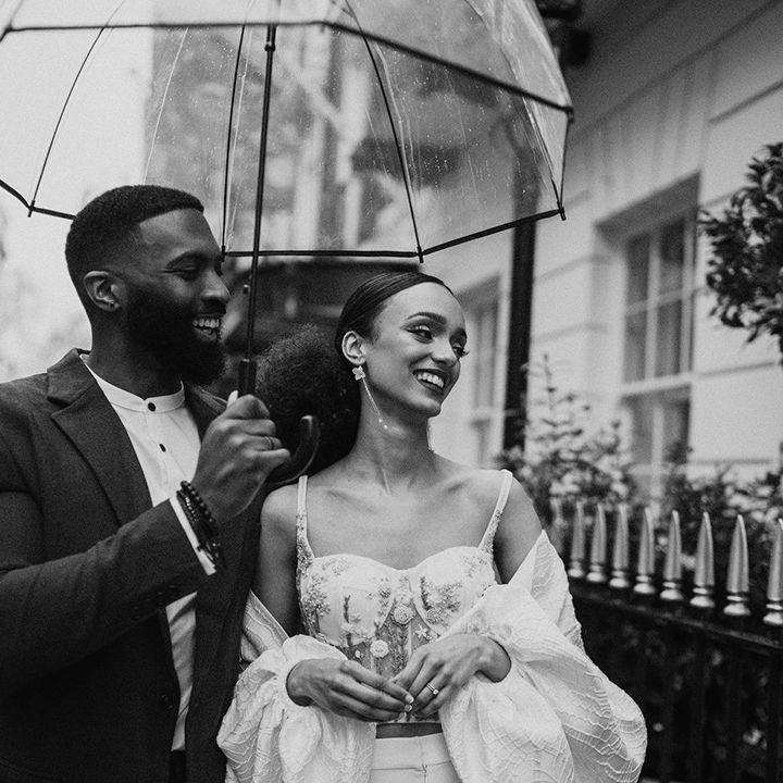 Black bride and groom standing under a clear umbrella at their intimate city wedding 