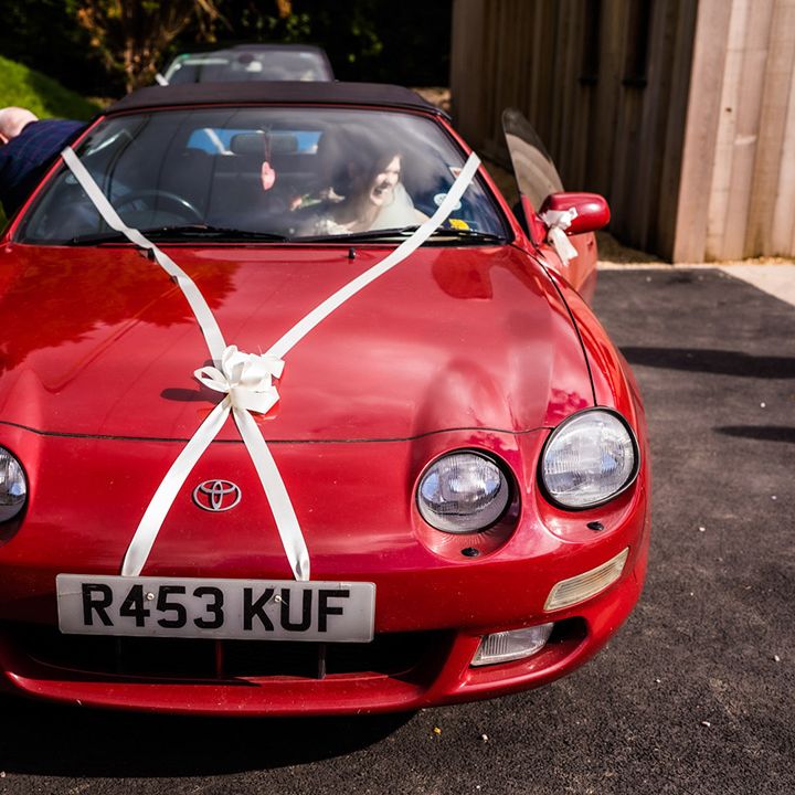 Bride in bright red vintage Toyota wedding car transportation with white ribbon