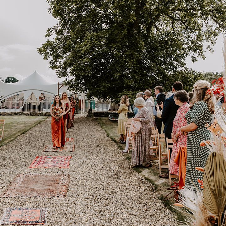 Bridesmaids walk down the aisle wearing Autumnal colour bridesmaid dresses in different styles 