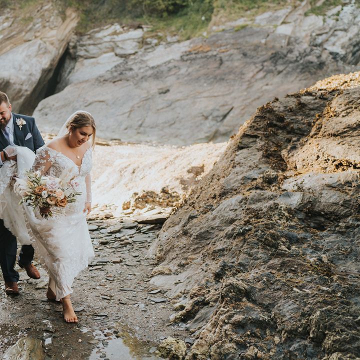 Groom holds brides wedding dress train for couples portraits beside the sea 