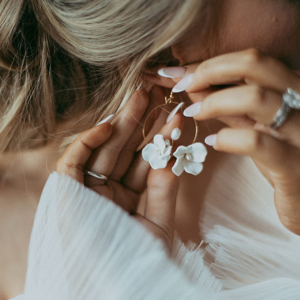Bride putting in gold hoop earring with small dainty white rose and pearl detail in the middle